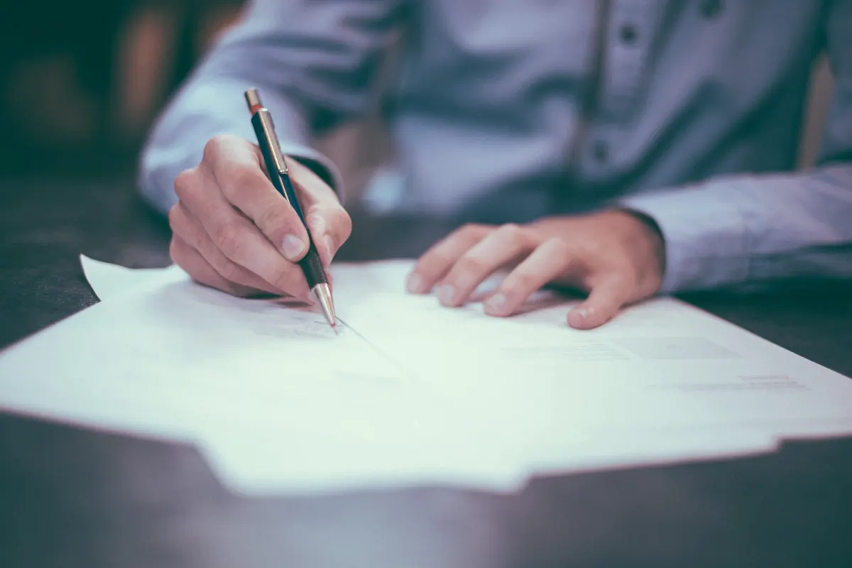 Persona firmando con bolígrafo un contrato sobre una mesa