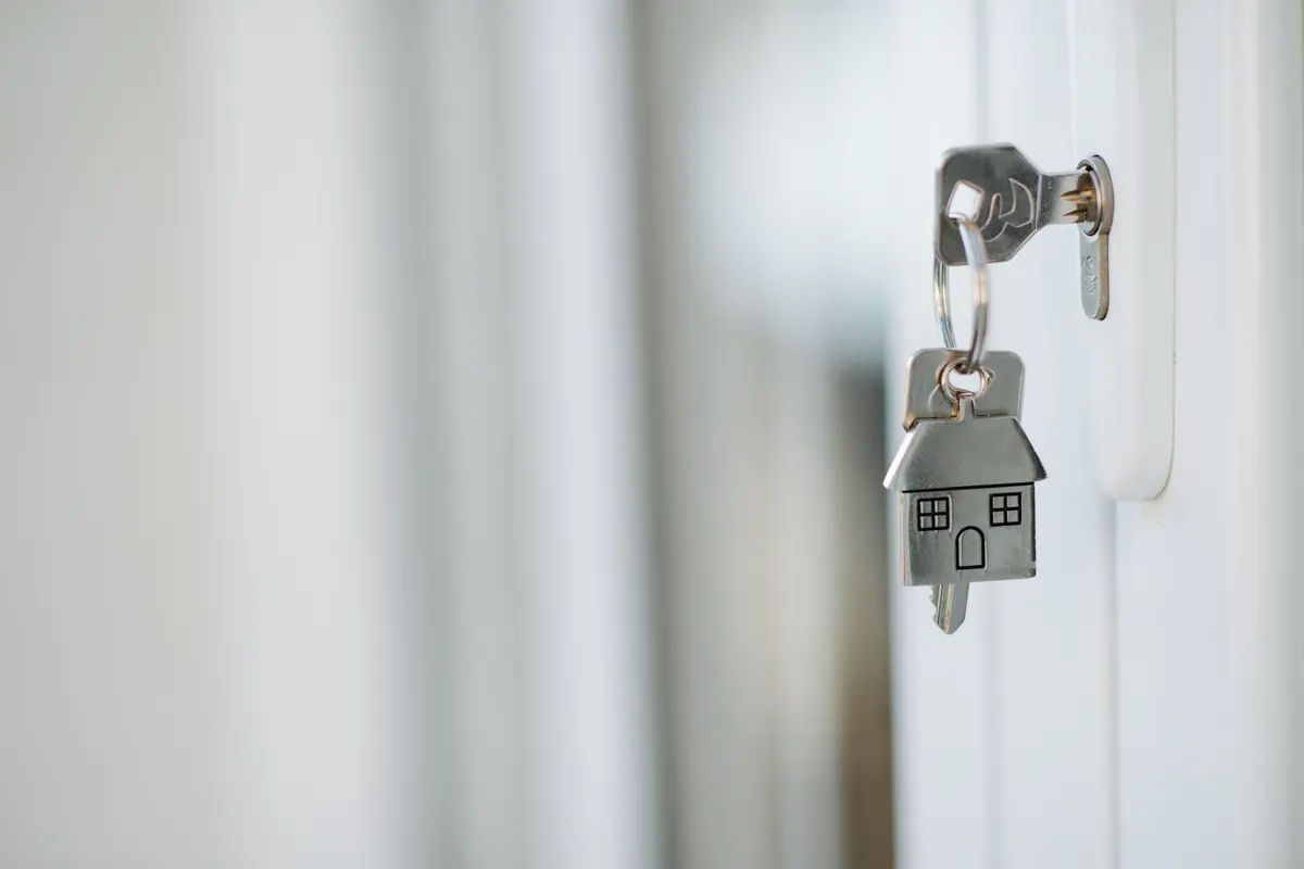 Llave con llavero en forma de casa puesta en la cerradura de una puerta blanca